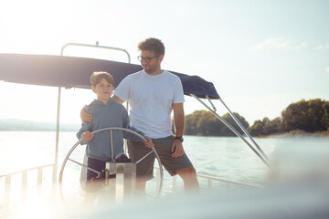 Father and son together steer a ship sailing on a river