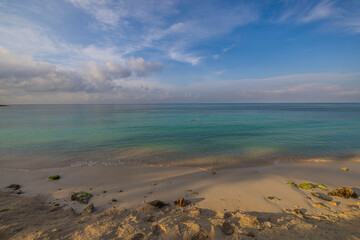 Gorgeous view sandy coastline and turquoise Atlantic ocean water surface merging with white clouds on horizon. Aruba. 