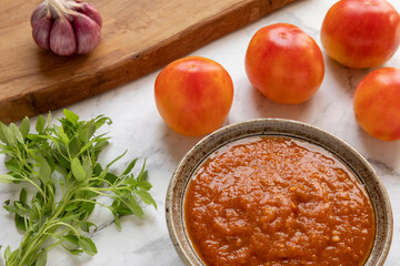 Fresh tomato basil sauce in bowl. Tomatoes, garlic bulb and greek piccolino  basil springs.