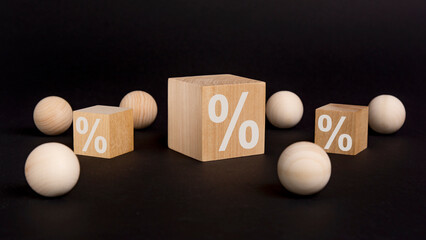 percent sign on wooden cube on black background with wooden balls. concept of sale and discount.