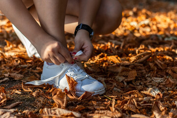 Close up of one sportswoman tying a shoelace outdoors in public park in autumn - obrazy, fototapety, plakaty