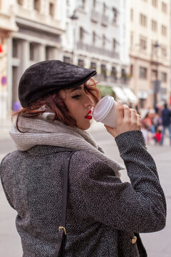 Mujer caminando por Madrid con un café en la mano y la bufanda en el cuello en pleno invierno.