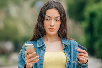girl with credit card and mobile phone or smartphone in the street with a surprised expression