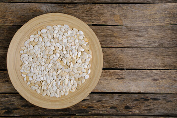 Pumpkin seeds in wooden plate on wooden background.