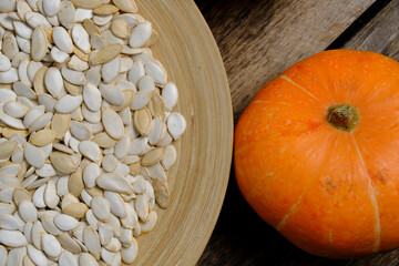 Pumpkins and pumpkin seeds in plate on wooden background.