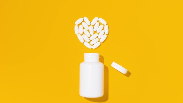 White pills in heart shape with bottle on yellow background. Mockup for advertising or other ideas. Medical and healthcare concept. Stop Motion Animation. 
