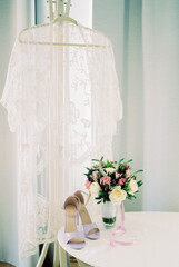 Lace robe hangs on a hanger near a table with a bouquet of flowers