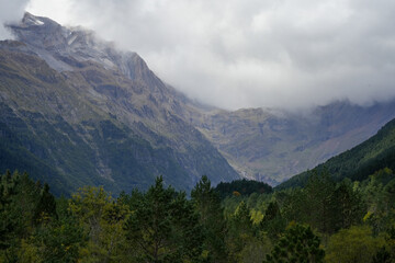 view along a glacial forest lined valley to a massive mountainous amphitheater (cirque) with cloud forming on the mountain tops  