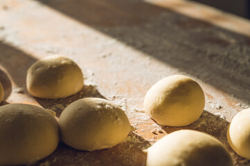 Close-up of raw dough balls and flour on wooden counter. Ready for baking. Sunlight.