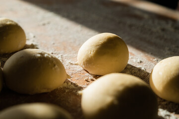 Close-up of raw dough balls and flour on wooden counter. Ready for baking. Sunlight.
