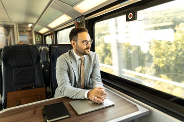 Young business man traveling to work by train. 
Working while traveling, using laptop, mobile phone and notebook
Thinking about new goals, noting, planning work