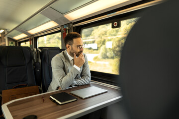 Young business man traveling to work by train. 
Working while traveling, using laptop, mobile phone and notebook
Thinking about new goals, noting, planning work