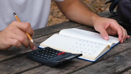 Man hand using a calculator and taking notes on a notebook, working outdoor concept video, calculating by using calculator - Powered by Adobe