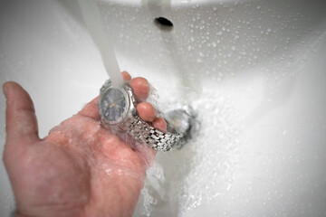 Checking the watch for water resistance. A man's hand holds a mechanical watch under a jet of water...