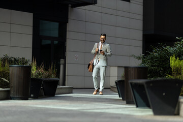 Business man in front of modern office building Business man walking of his office and using mobile phone