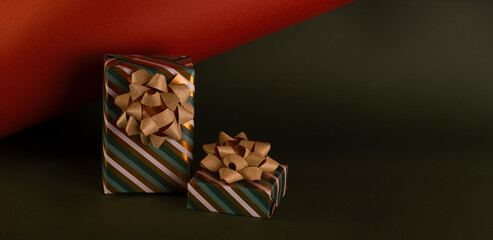 Boxing Day concept with gift boxes in gold and green colors decorated with sparkling bow against deep green and brick color background.