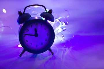 alarm clock on the background of garlands. Purple background. A new year is coming.