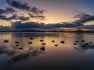 Fototapeta premium Aerial sunrise waterscape with boats, rain clouds and reflections