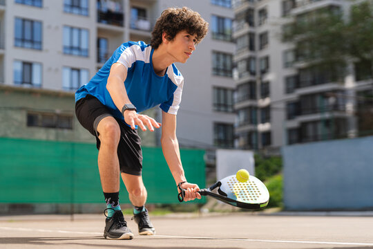 Sportive young boy with racquet playing padel in the open court outdoors