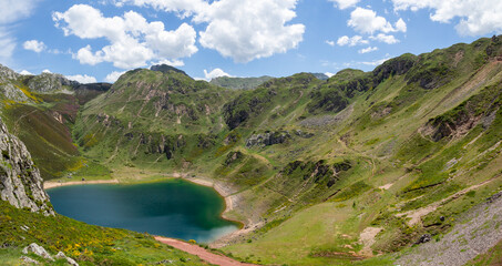 Fototapeta na wymiar Vistas del paisaje asturiano del Lago de La Cueva por un sendero rodeado de naturaleza, montañas verdes, flores moradas cielo azul y nubes blancas en verano de 2021, España. 