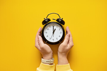 Daylight saving day. Fall Back. Black Alarm clock and female hands on yellow background. Daylight...