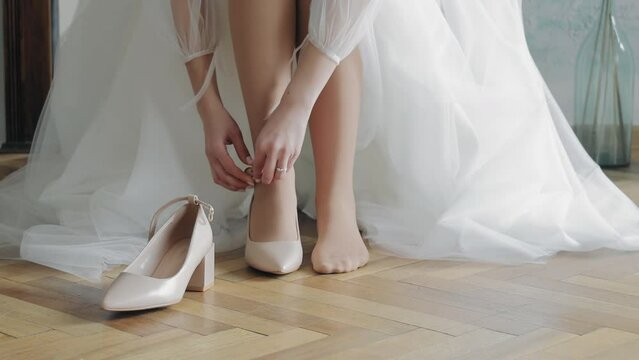 the bride puts on her shoe on her wedding day. A white shoe on a girl's fragile leg.
