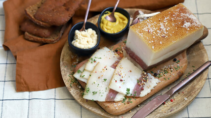 Fresh lard with meat layer on a wooden board with spices, mustard and horseradish. Delicious snack. Bacon.