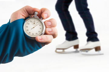 measuring speed on skates with a stopwatch. hand with a stopwatch on the background of the legs of a man skating on an ice rink