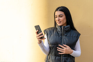 Young woman with long brunette hair looking at the phone smiling on yellow background