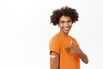 Obraz na płótnie Canvas Portrait of hispanic young man smiling, showing his vaccine shot from covid-19, vaccination campaign from coronavirus pandemic, standing over white background