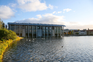 Reykjavik City Hall (Ráðhús Reykjavíkur in Icelandic) over Lake Tjornin on a sunny day with a cloudy blue sky.  Image has copy space.
