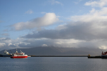Fototapeta premium A lone red cruise ship on the water under a dramatic cloudy sky off the coast of Reykjavik, Iceland. Image has copy space.