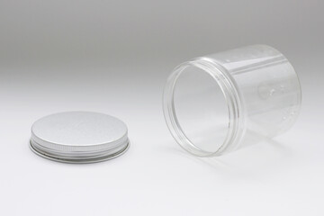 Opened lying plastic jar with drops of water, horizontal photo on light background. Decorative design element, empty storage container, gray cover lies nearby