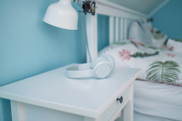 White wireless headphones lie on the bedside table near the bed in hotel room. Wood bedside table. 