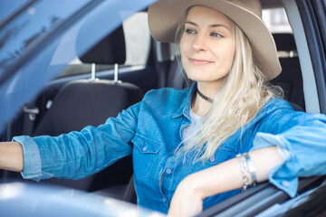 Pretty woman joyfully leave city driving car sticking elbow out open window. Young blonde lady in...