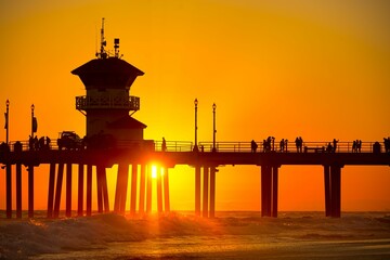 Silhouette eines Piers mit Wanderern unter einem orangefarbenen Sonnenuntergangshimmel am Huntington Beach, Kalifornien
