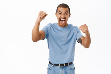 Naklejka premium Enthusiastic arab guy shouting, cheering, watching sports game and rooting for team, standing over white background