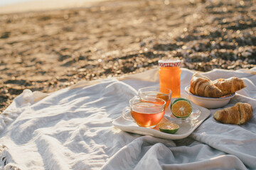 Tasty summer picnic with fresh tea and croissants on the beach at sunset.