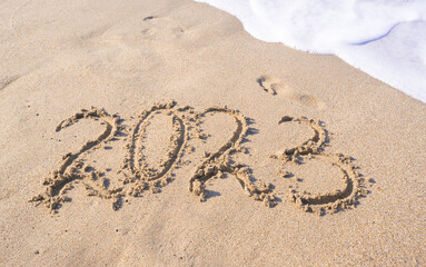 The year 2023 is written in the sand on the sea beach.