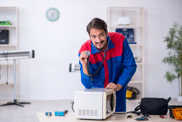 Young male repairman repairing oven at workshop