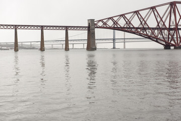 Obraz premium View of the George IV Bridge Rail Bridge from the distance across the Firth of Forth in an overcast Winter day in Edinburgh, Scotland, UK, with the Queensferry Crossing on the background