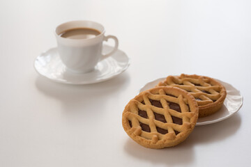 Crostate al cioccolato con tazzina bianca di caffè su tavolo bianco