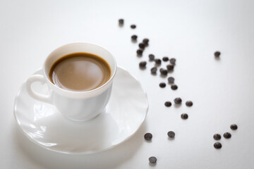 Tazza bianca con caffè e piattino con chicchi di cioccolato su tavolo bianco