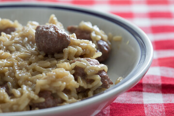 Piatto di risotto con salsiccia su tovaglia bianca e rossa a quadri