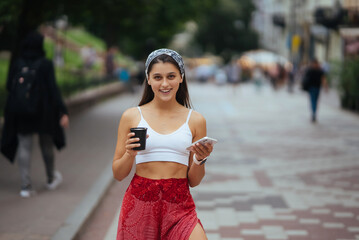 Woman in the street drinking morning coffee and use smartphone.