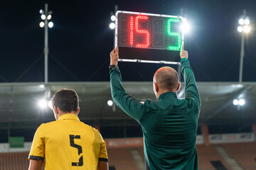 Sideline referee shows players substitution during football match.