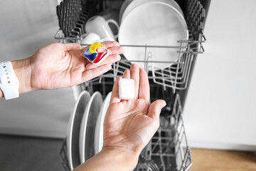 Choice between gel capsule and powder. Open dishwasher in a white kitchen. gel capsules for dishwashers. Dishwasher capsule. Brilliant cleanliness.