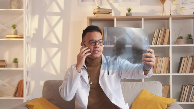 Doctor call. Mobile medical consulting. Remote healthcare. Male physician studying chest X-ray film speaking to patient on phone at modern home interior.