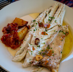 Eating in restaurant of fresh grilled on old charcoal parrillas sea bass fish in small fisherman's village Getaria, Basque Country, Spain
