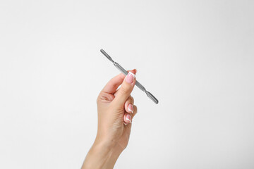 A girl with beautiful long nails holds a curette for manicure on a white background